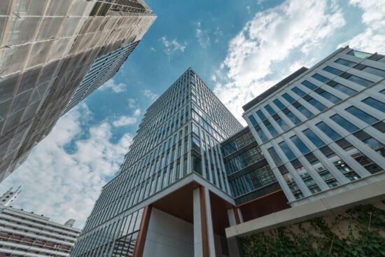 Low-angle view of modern glass office buildings against a partly cloudy blue sky in an urban setting.